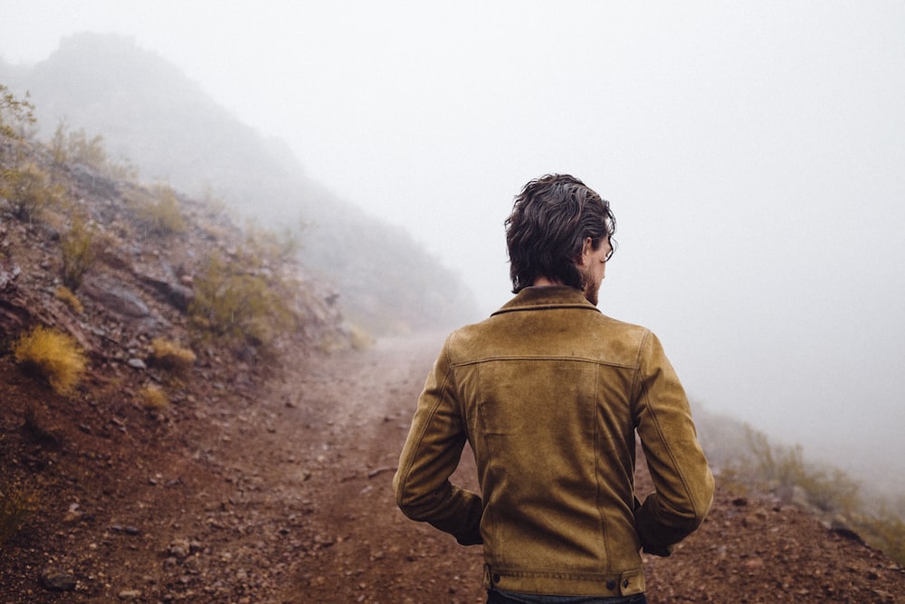 person wearing brown jacket standing near hill