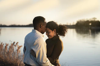 man and woman facing each other while hugging and standing near body of water during daytime