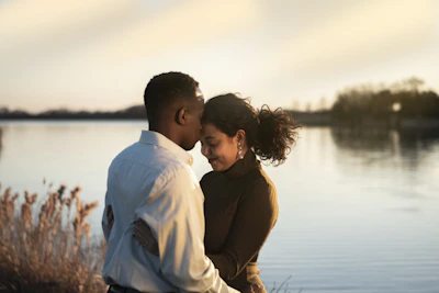 man and woman facing each other while hugging and standing near body of water during daytime
