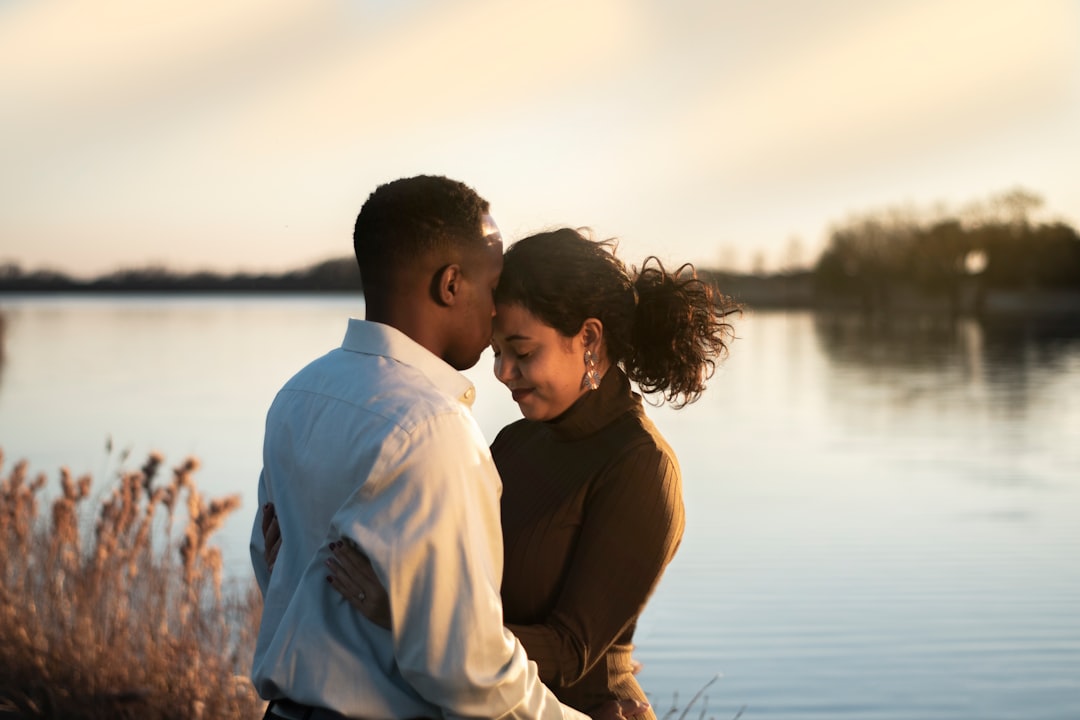 man and woman facing each other while hugging and standing near body of water during daytime