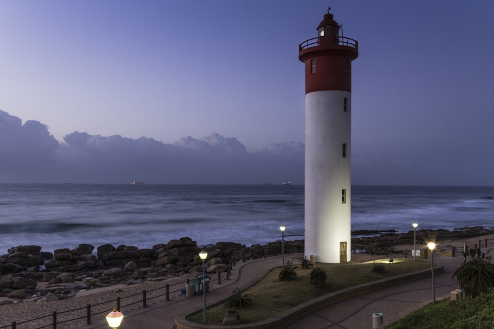 farol branco e vermelho perto do oceano durante o dia