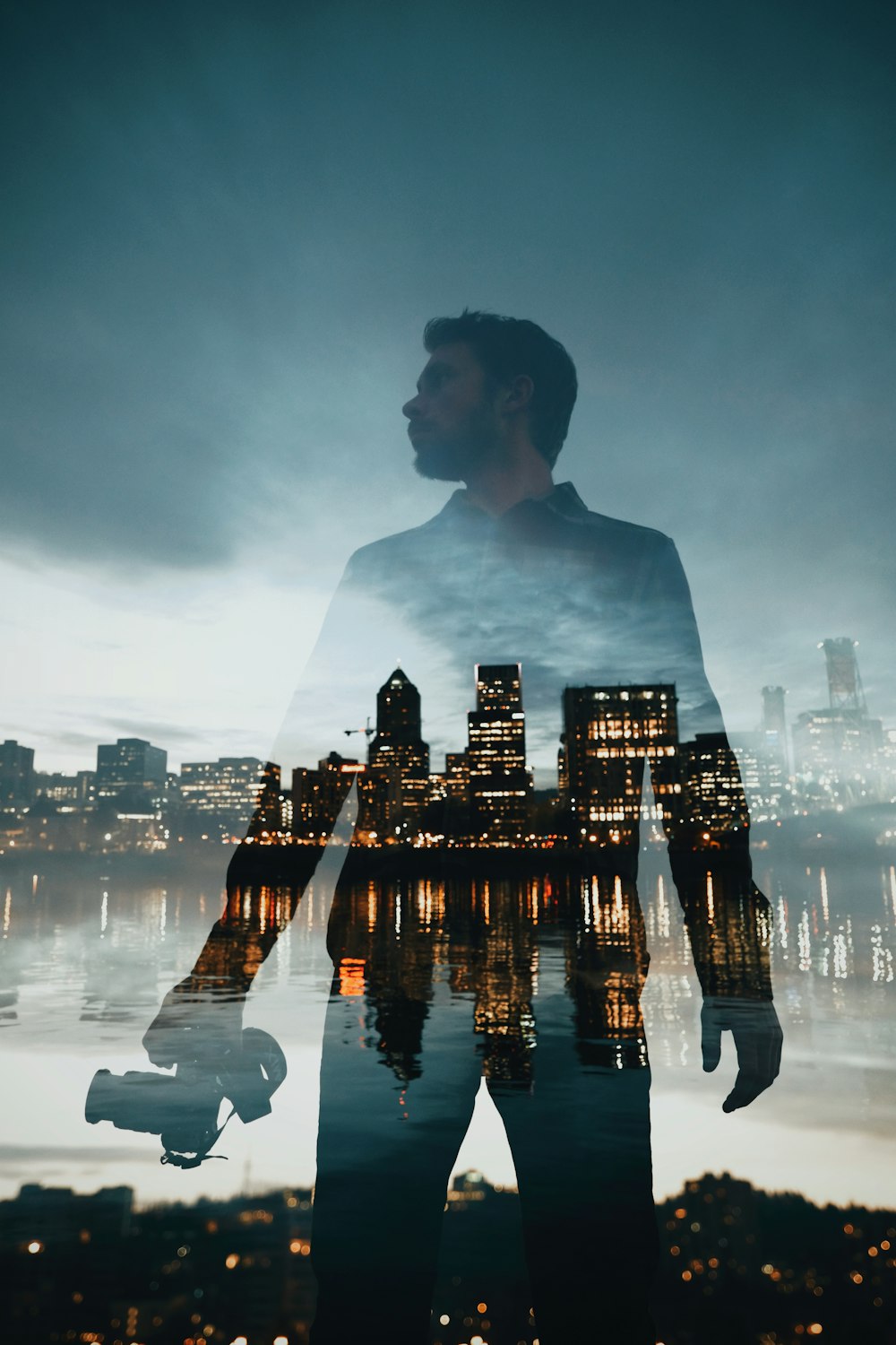 city with high-rise buildings near body of water with the reflection of man standing holding camera