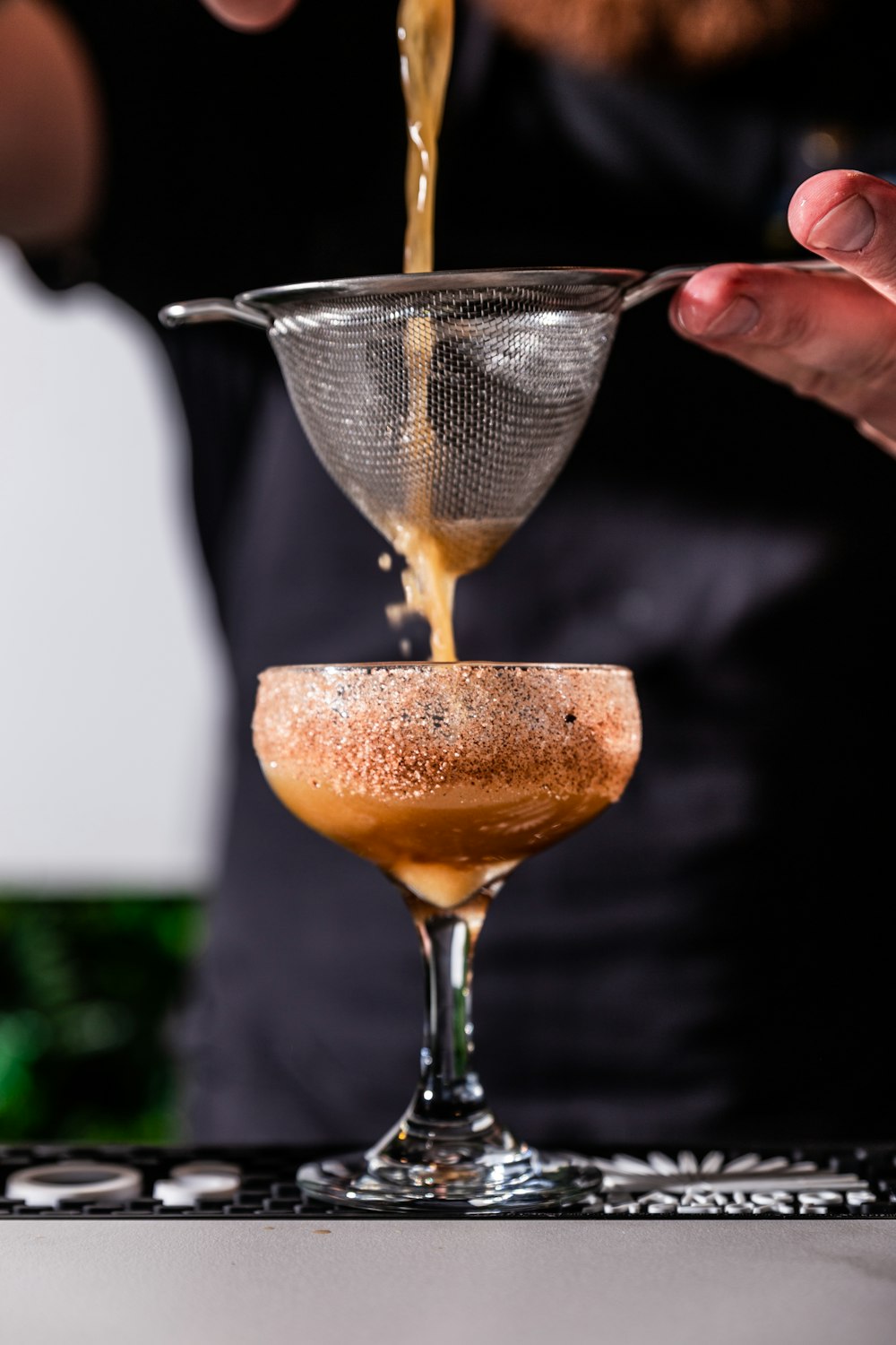 person holding strainer while pouring juice on glass flute