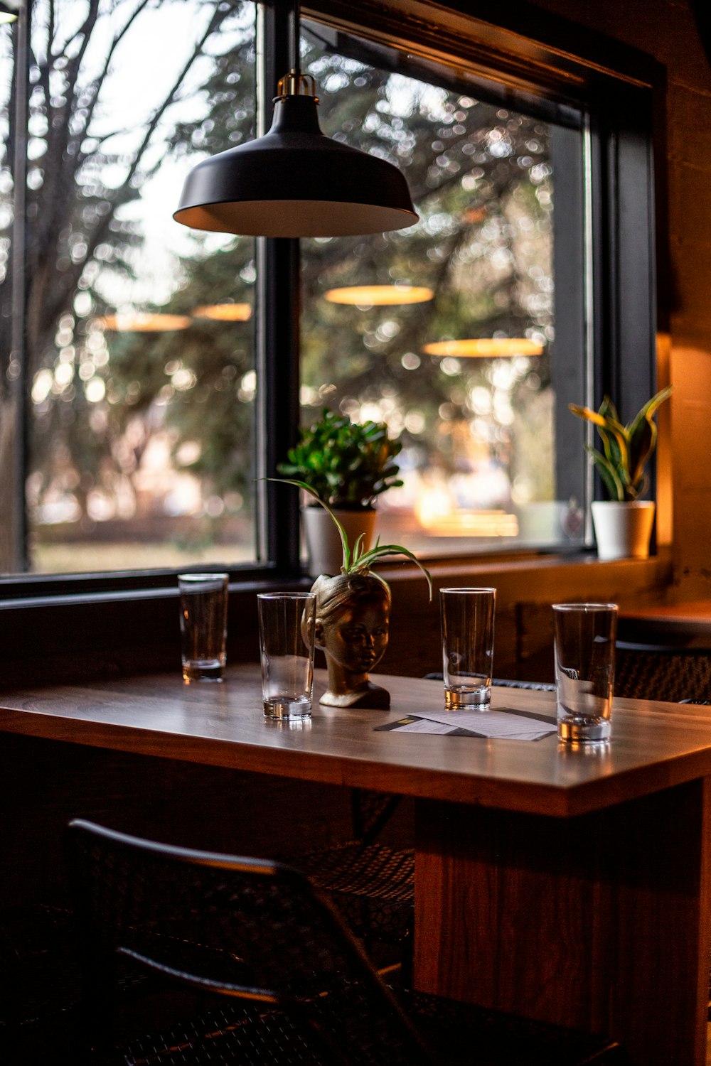 Vasos transparentes de base redonda sobre mesa de madera marrón y lámpara colgante redonda en blanco y negro