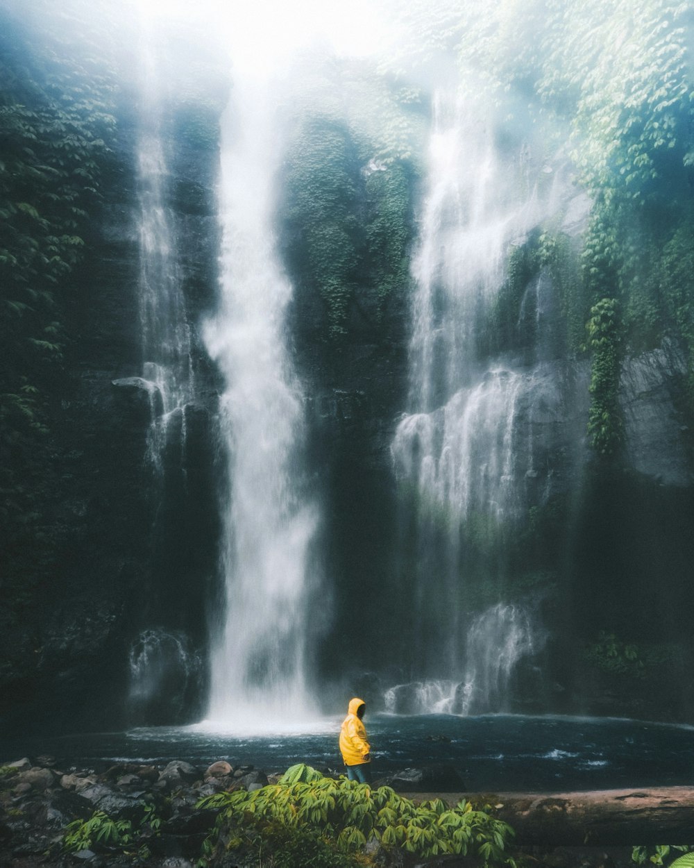 person wearing yellow hooded jacket standing near waterfalls