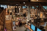 An expansive bookstore with multiple levels and wooden bookshelves filled with a variety of books. People are browsing and walking around the store. The space is well-lit with overhead lights, and there are some plants placed strategically to enhance the atmosphere.