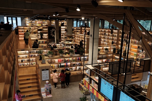 An expansive bookstore with multiple levels and wooden bookshelves filled with a variety of books. People are browsing and walking around the store. The space is well-lit with overhead lights, and there are some plants placed strategically to enhance the atmosphere.