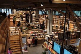 An expansive bookstore with multiple levels and wooden bookshelves filled with a variety of books. People are browsing and walking around the store. The space is well-lit with overhead lights, and there are some plants placed strategically to enhance the atmosphere.