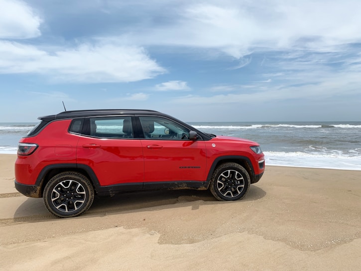 A sleek navy blue SUV parked on a sandy beach with crystal-clear waves in the background.