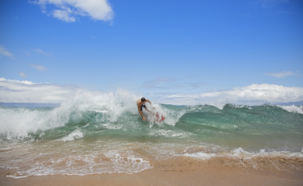 topless man surfing on sea wave under blue and white sky