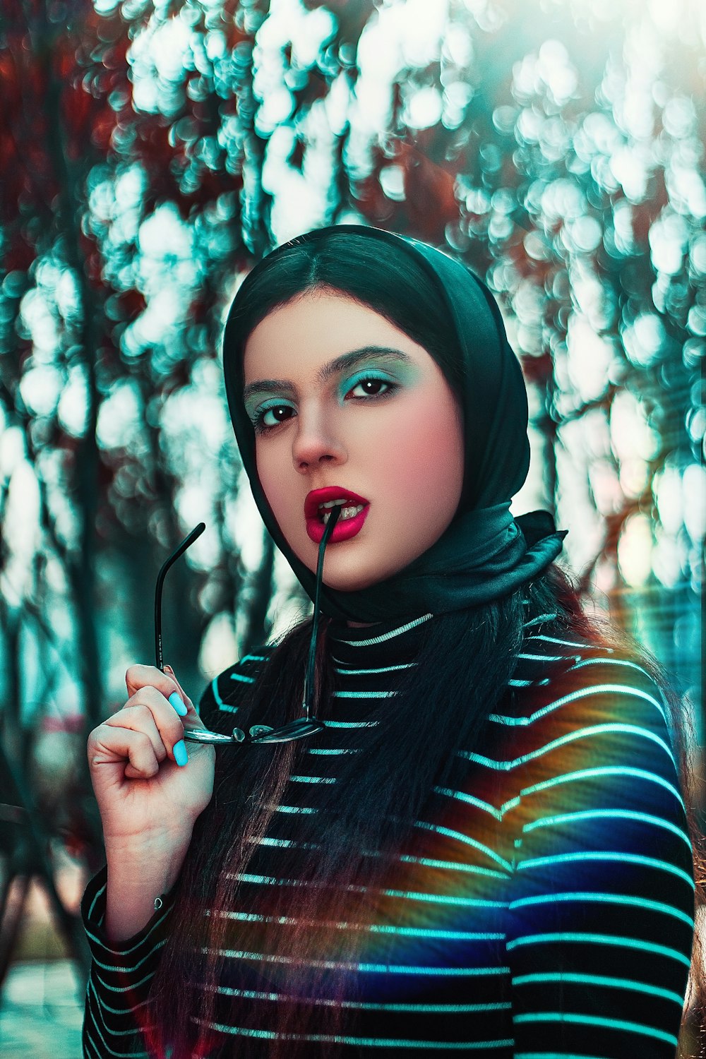 woman in black, white, and blue striped top biting eyeglasses