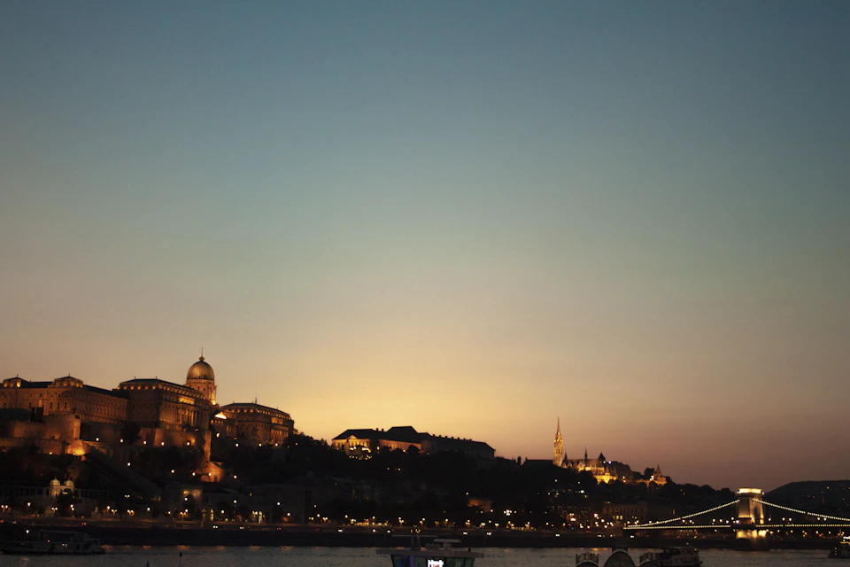 Buda Castle illuminated by warm orange and yellow lights at night along Danube River
