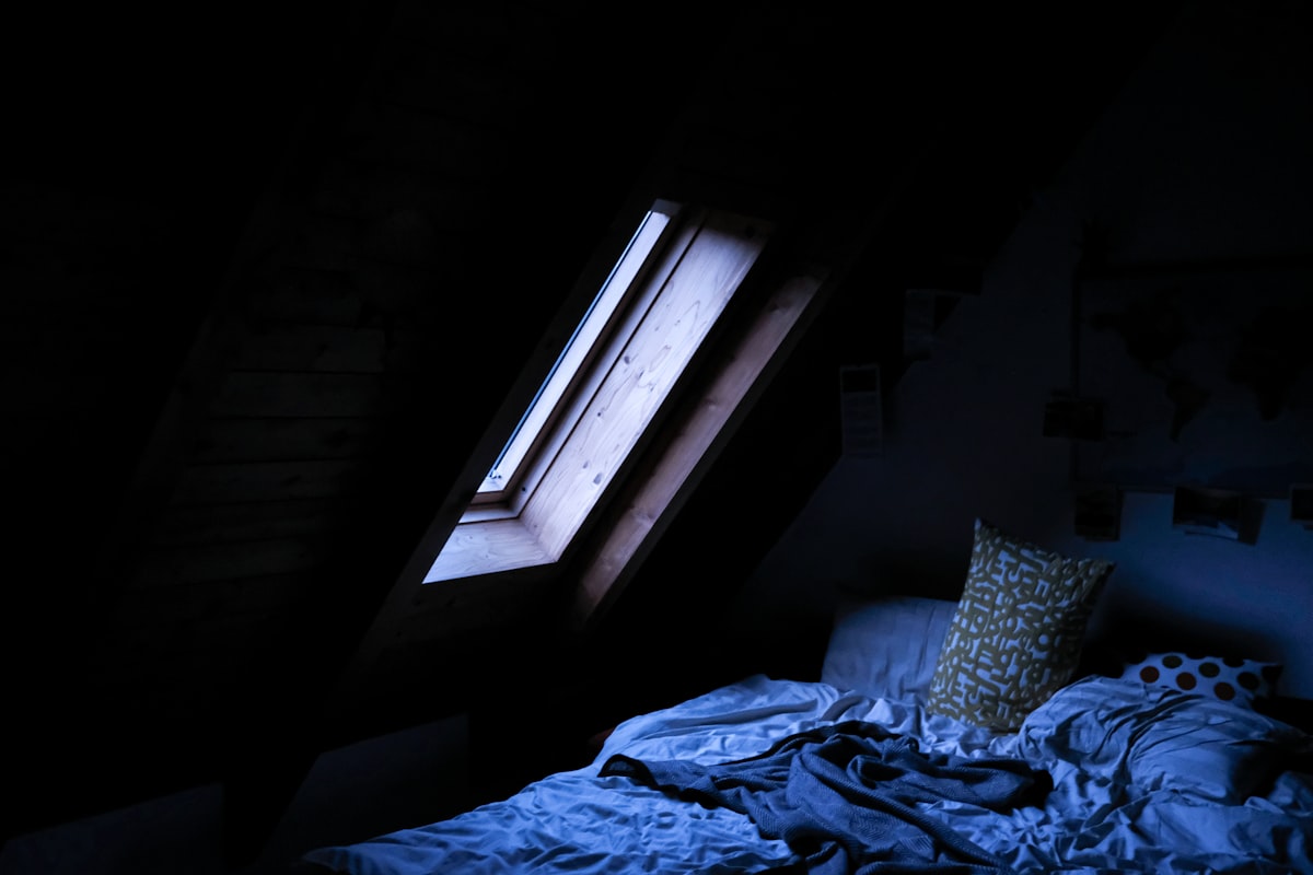 Soft light falling across an unmade bed in a dark room, evoking restful sleep and recovery