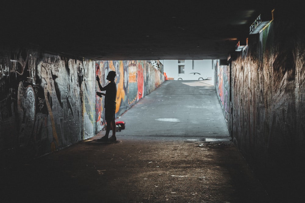 person standing inside tunnel with murals