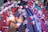 An umbrella is adorned with various colorful ribbons, bows, flowers, and small flags featuring a blue canton with a white sun. The decorations include red, white, and blue elements, as well as tassels and small cartoon figures. The items are neatly arranged in patterned rows across the umbrella's surface.