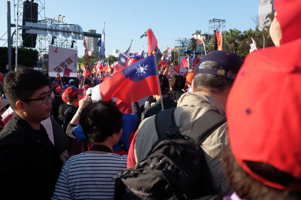 A lively rally with members holding banners and flags under a bright blue sky.