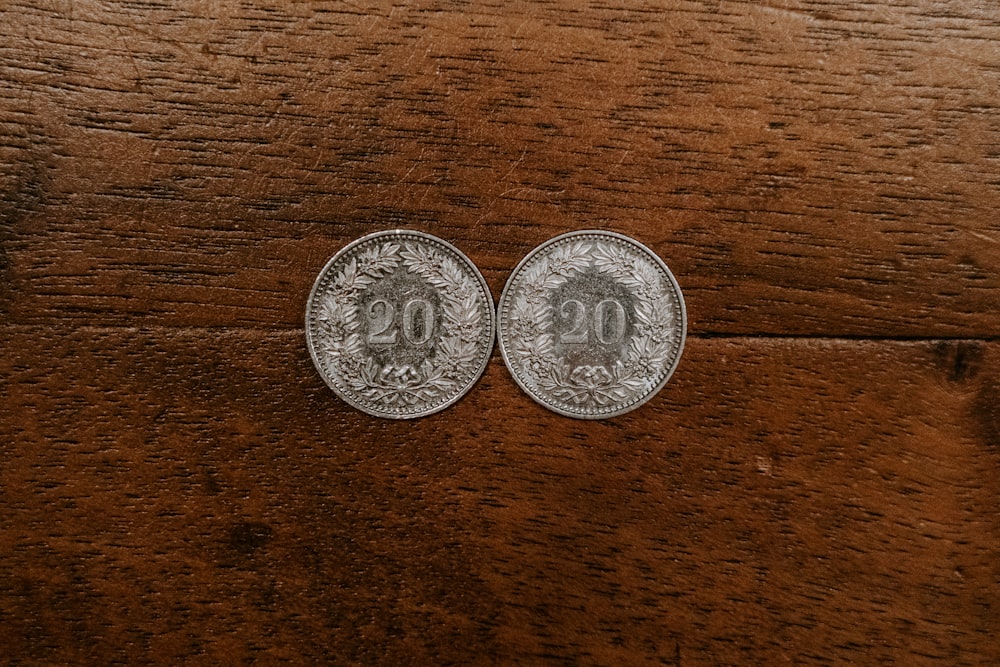 two round silver-colored 20 coins on brown surface