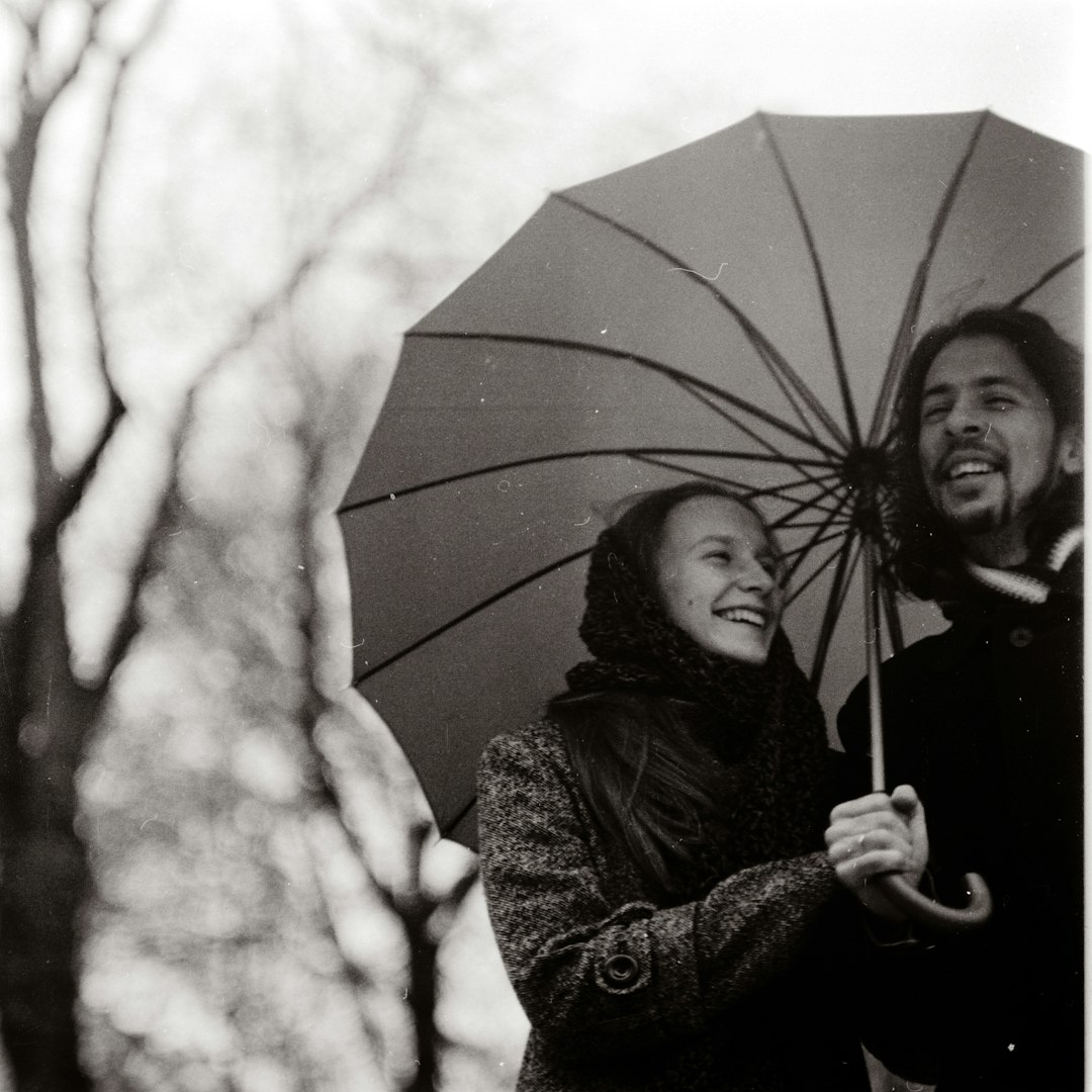 grayscale photography of man and woman holding cane umbrella outdoors