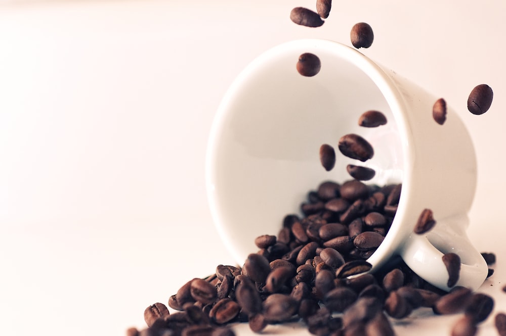 a white cup filled with coffee beans on top of a table