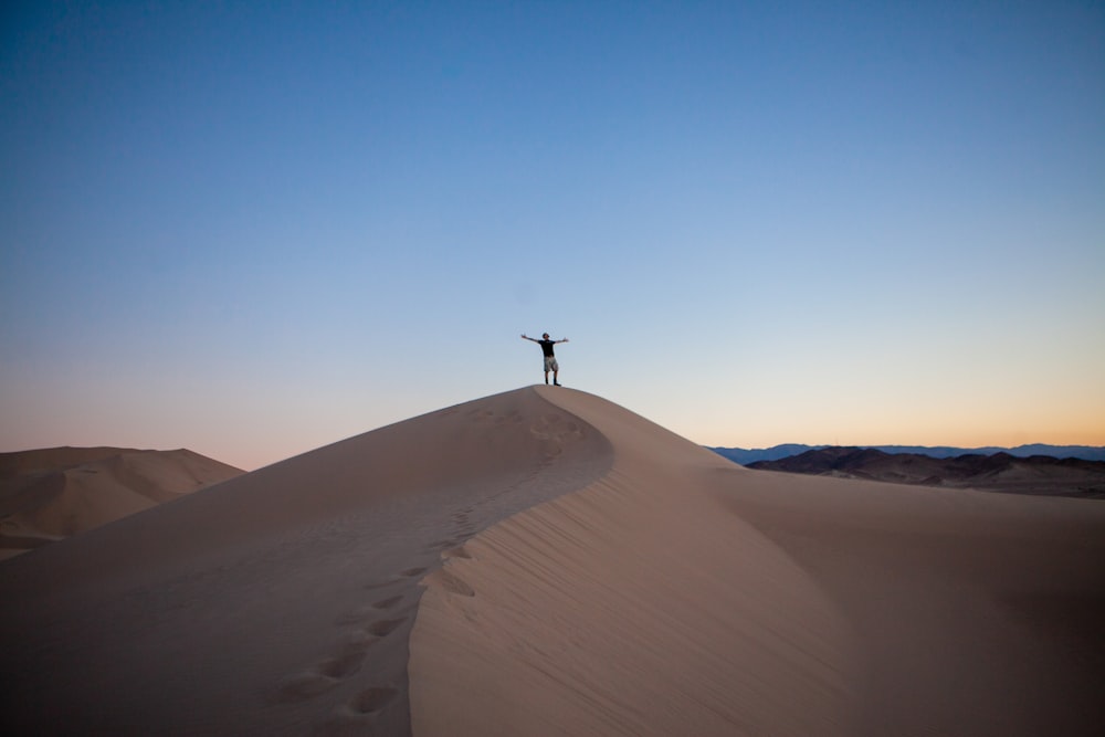 person raising both hands while standing on desert under blue and white sky