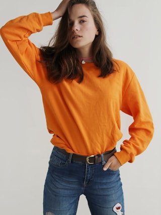 woman wearing orange crew-neck sweatshirt standing while putting right hand on her head