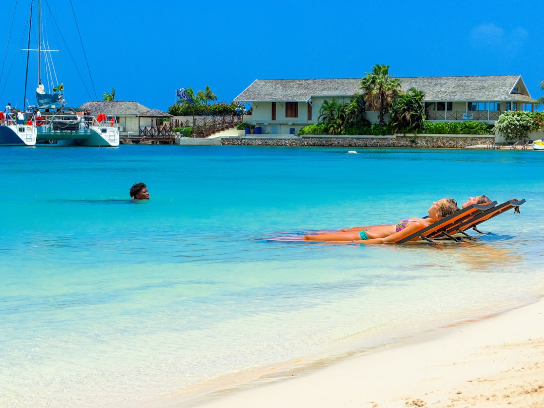 Two women sunbathe while a man swims in the ocean off the coast of Jamaica