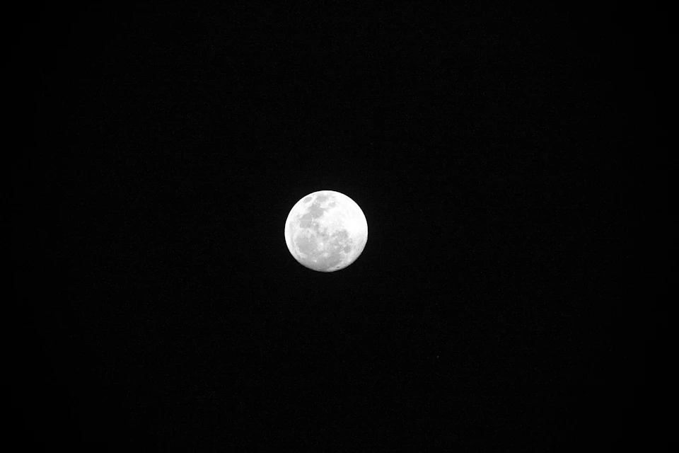 The image depicts a full moon, round and white in color, positioned centrally against a black sky. The moon is surrounded by an expanse of darkness, creating a stark contrast with its luminosity. The perspective of the photo is from below, looking up at the moon, which adds to the sense of awe and wonder it evokes.