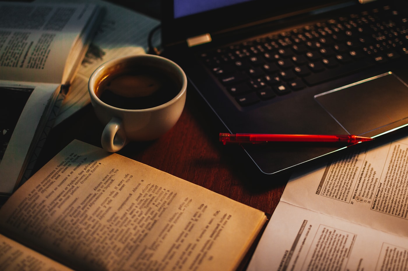A close-up photograph displays aged parchment sheets laid out directly next to a closed silver laptop on a polished office table.