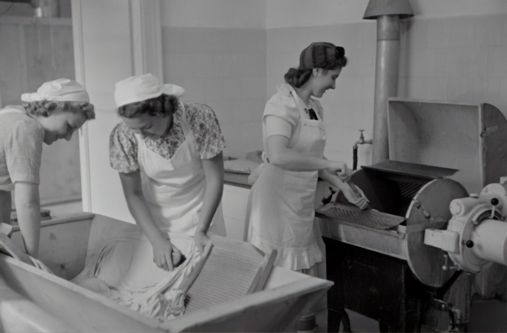 grayscale photography of three women washing clothes