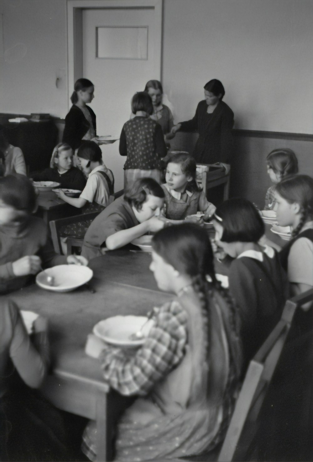 Photographie en niveaux de gris d’enfants assis tout en mangeant près d’une table