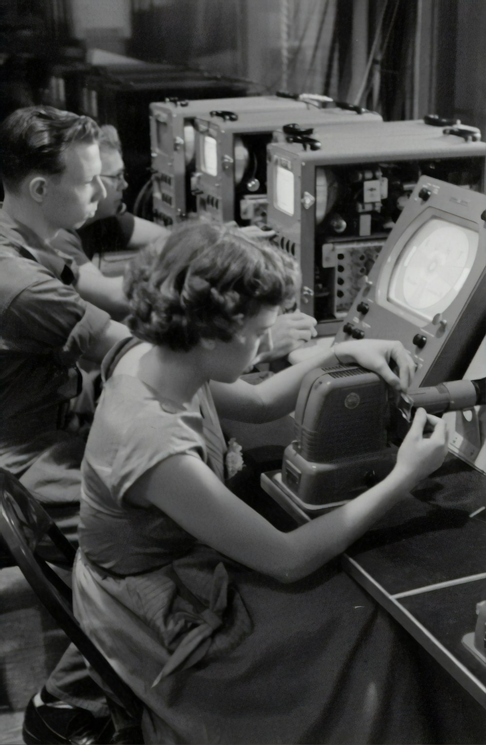Photographie en niveaux de gris de trois personnes assises près d’écrans