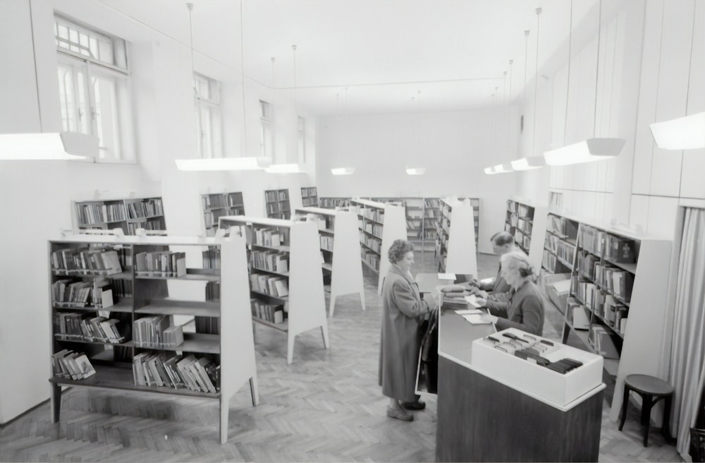 fotografia in scala di grigi di persone all'interno della libreria