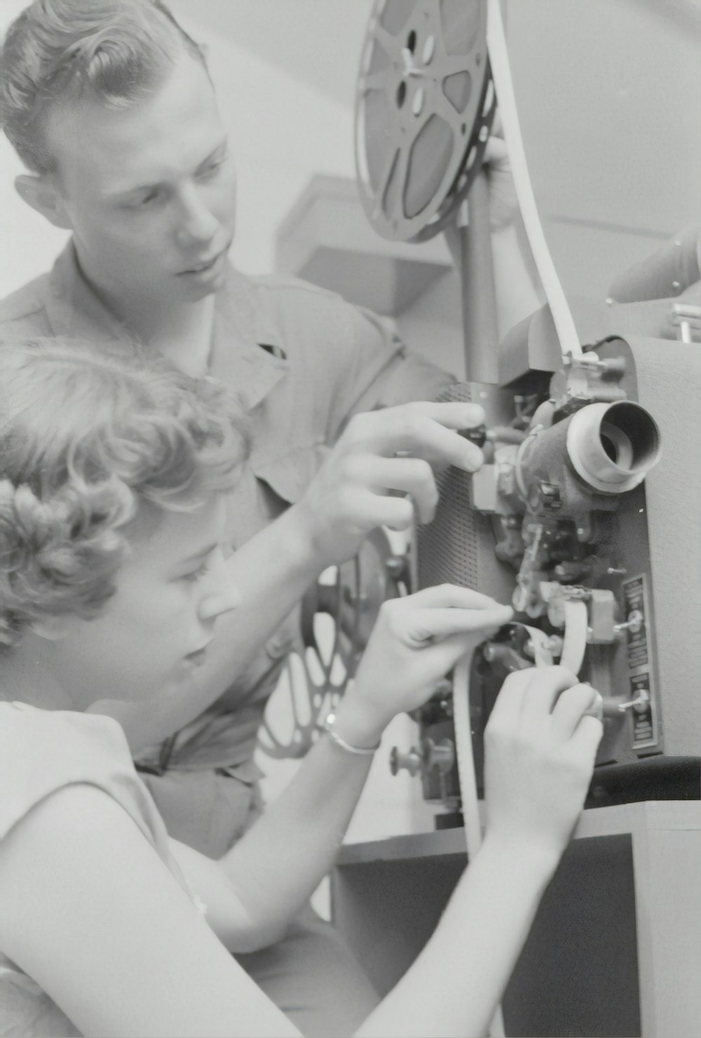 grayscale photography of man standing near woman sitting while fixing electronic component