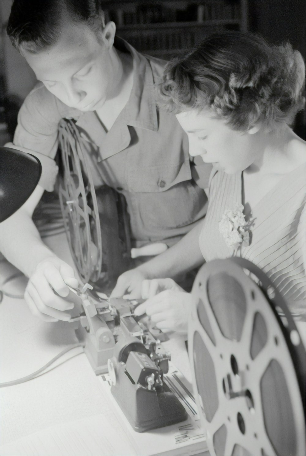 fotografia in scala di grigi dell'uomo che assiste la donna mentre ripara la bobina della pellicola
