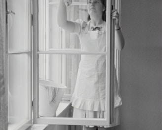 grayscale photography of woman cleaning glass window