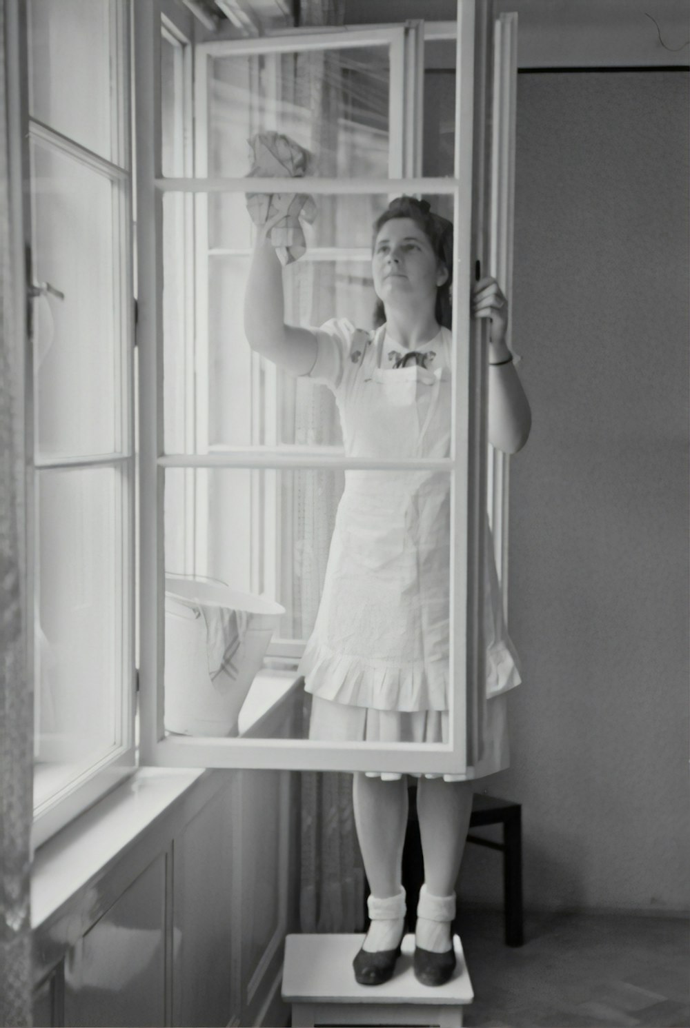fotografia in scala di grigi della donna che pulisce la finestra di vetro