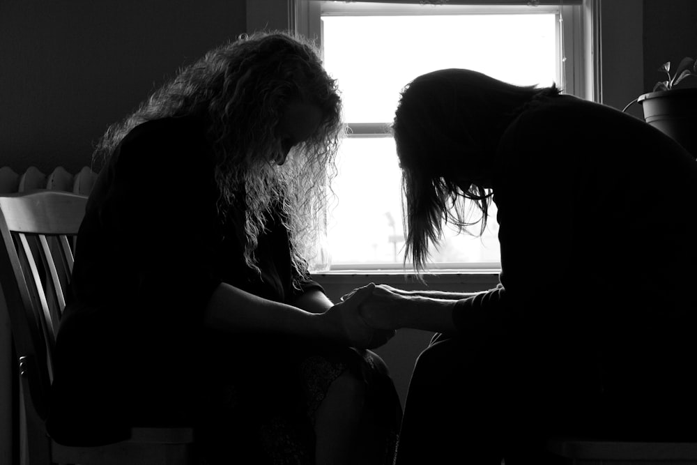 two sitting women holding hands each other while praying inside room