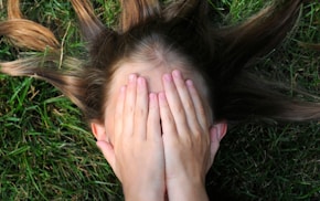 woman covering her face lying on green grass