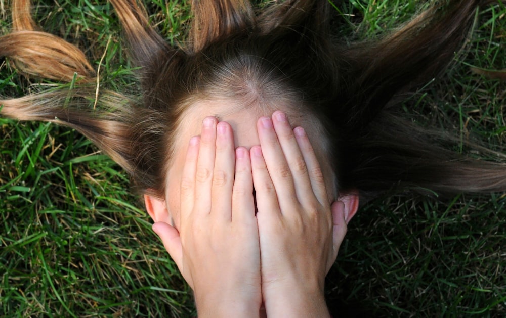 woman covering her face lying on green grass