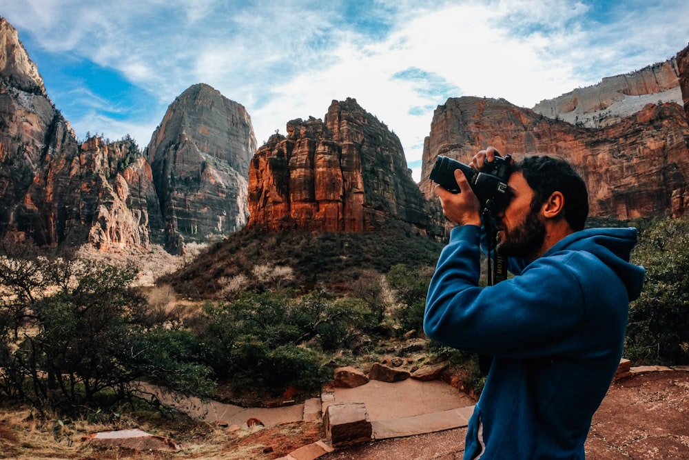 man using DSLR camera near shrubs and mountains during day
