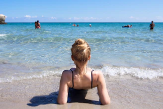 a woman sitting on the beach looking at the water