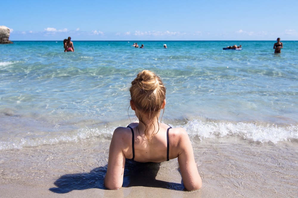 a woman sitting on the beach looking at the water