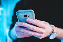 Close-up of hands holding a smartphone with vibrant accessories around.