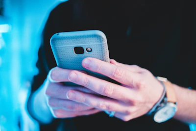 Close-up of hands holding a smartphone with vibrant accessories around.