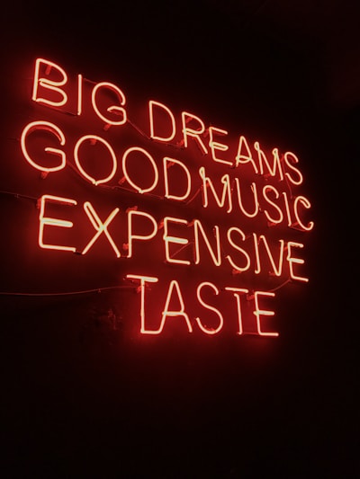 Neon sign displaying the phrases 'BIG DREAMS', 'GOOD MUSIC', 'EXPENSIVE TASTE' illuminated in bright red against a dark background.