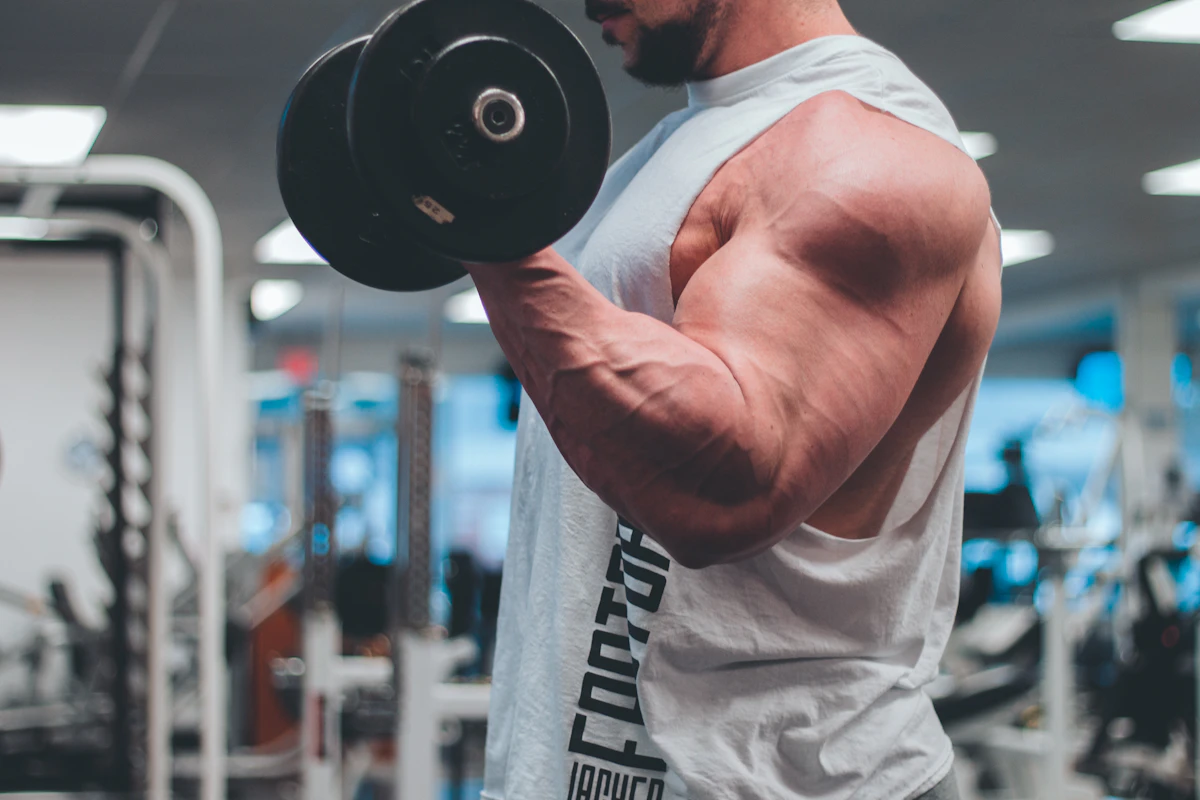 Man lifting a dumbbell in a white tank top, illustrating the strength and energy goals men weigh when comparing transdermal and injectable testosterone therapy.
