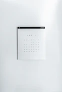 A simple wall calendar displays the month of January 2020 with dates arranged in a grid format. The calendar has a minimalistic design on a plain white wall, featuring a black strip across the top with the year '2020' printed on it.