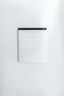 A simple wall calendar displays the month of January 2020 with dates arranged in a grid format. The calendar has a minimalistic design on a plain white wall, featuring a black strip across the top with the year '2020' printed on it.