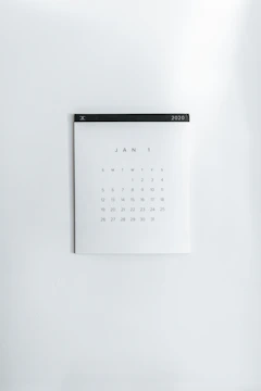 A simple wall calendar displays the month of January 2020 with dates arranged in a grid format. The calendar has a minimalistic design on a plain white wall, featuring a black strip across the top with the year '2020' printed on it.