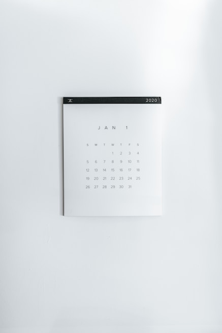 A simple wall calendar displays the month of January 2020 with dates arranged in a grid format. The calendar has a minimalistic design on a plain white wall, featuring a black strip across the top with the year '2020' printed on it.